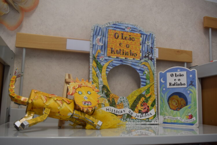 Capa produzida, com o leão junto ao livro original em exposição na biblioteca escolar.